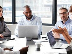 A group of people discuss something around a boardroom table