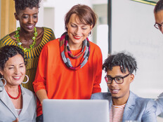 A group of smiling people gather around a laptop