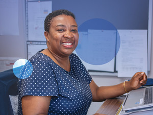 A woman smiles at the camera while working on her computer