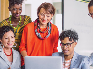 A group of smiling people gather around a laptop