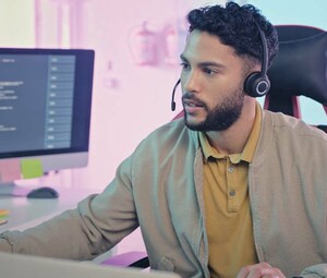 A man wearing a headset sits at a modern workstation with multiple monitors