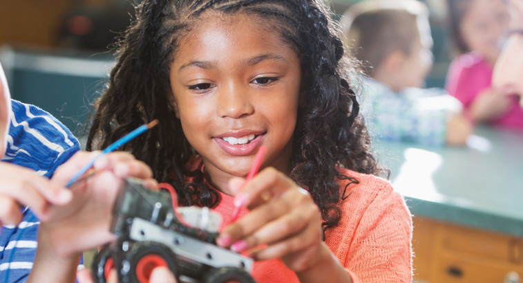Students engage in STEM lessons with a robotic car while smiling teacher looks on