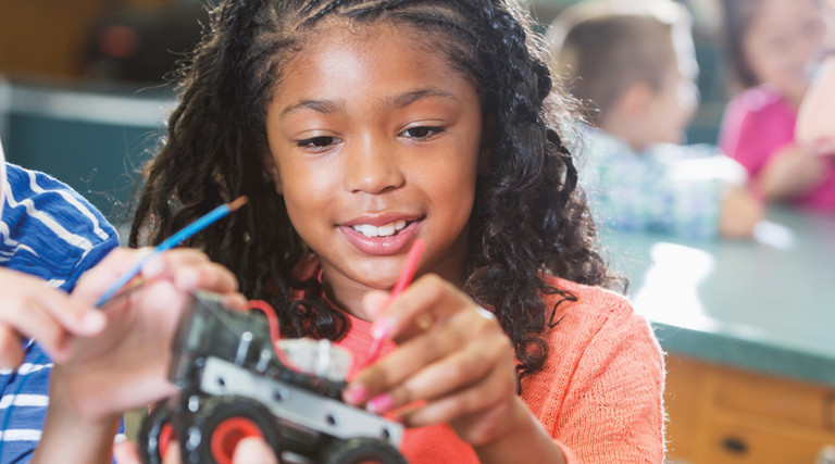 Students engage in STEM lessons with a robotic car while smiling teacher looks on