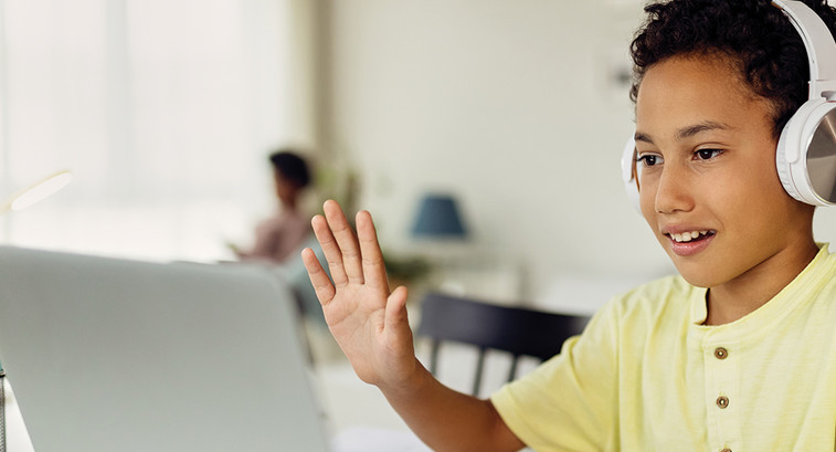 Young boy with headphones on waving at computer screen