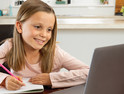 girl smiling and taking notes on paper while looking at computer screen