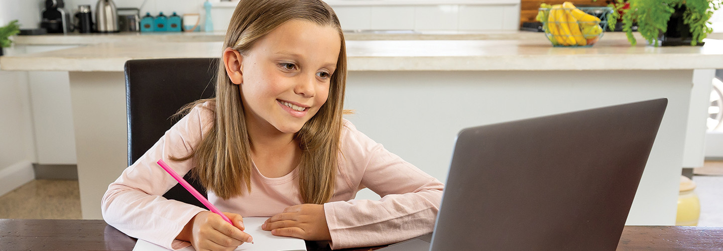 girl smiling and taking notes on paper while looking at computer screen