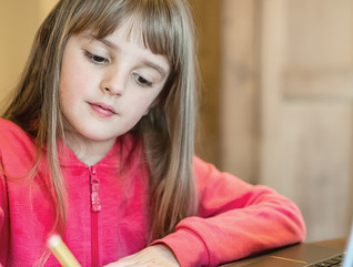 girl taking notes on paper from laptop for school