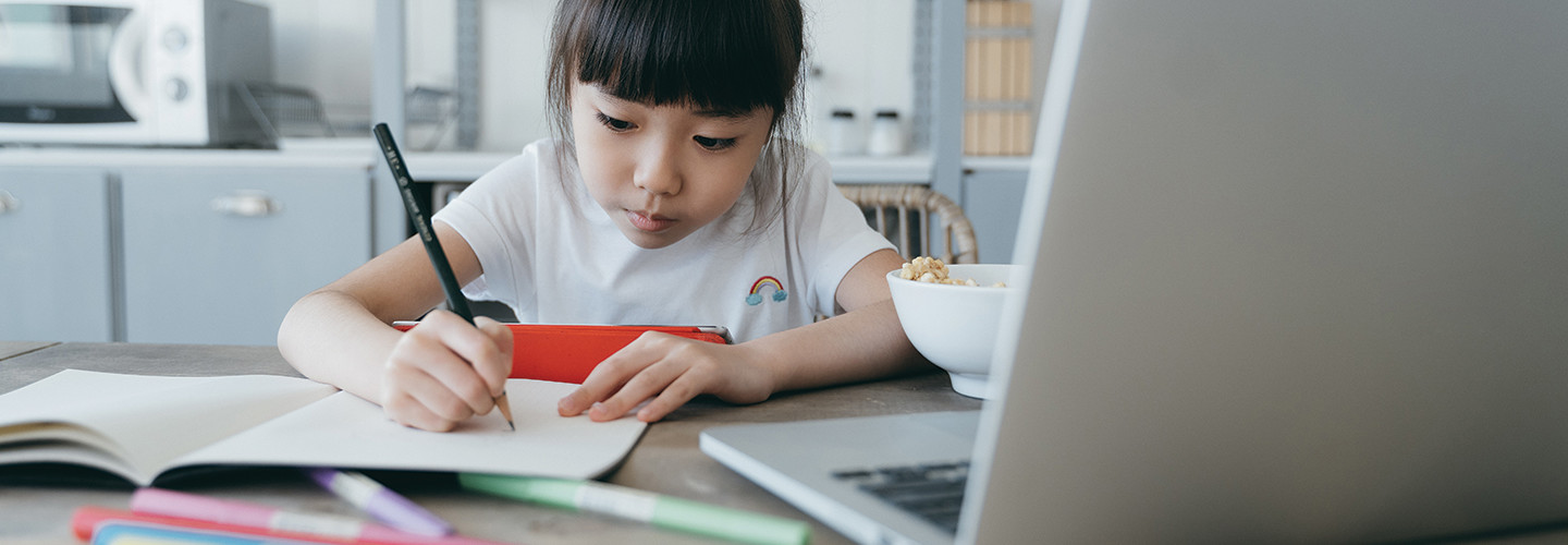 young girl taking notes on paper from computer while holding tablet 
