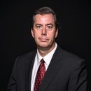 Photo of Wade Grant in black suit on black background with white shirt and red tie