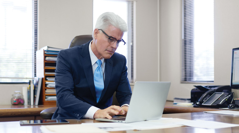 Administrator at desk looking at paperwork and laptop federal funding 