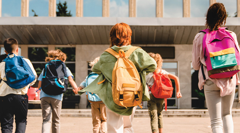 group of k-12 students with backpacks going into school building