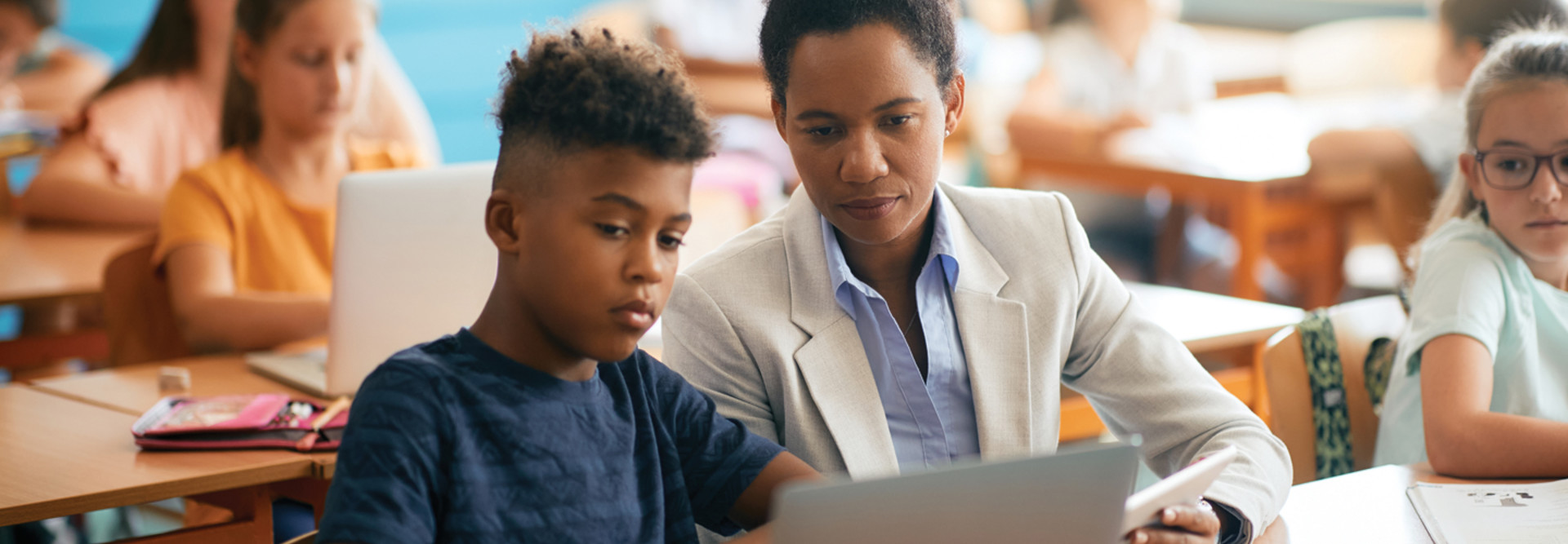 Educator working with student in classroom on laptop computer