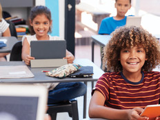 Students in classroom on tablets looking at teacher