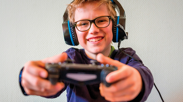 boy with glasses wearing headphones and holding gaming controller