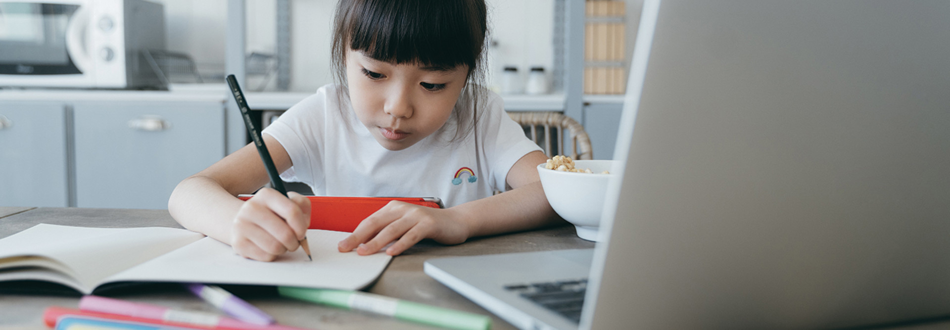 young girl taking notes on paper from computer while holding tablet 
