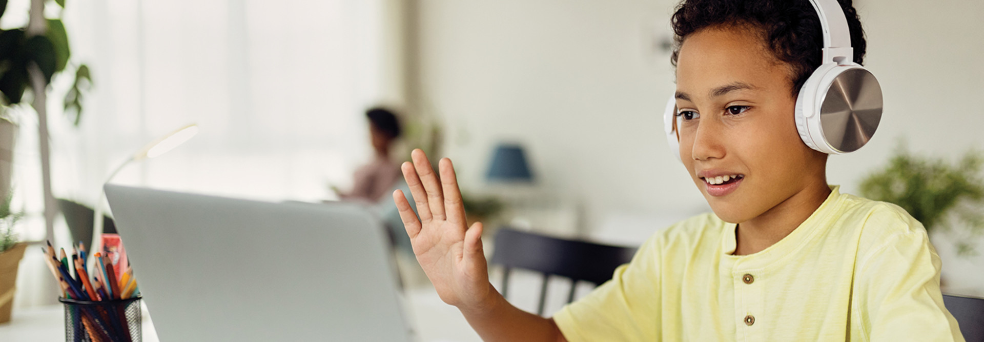 Young boy with headphones on waving at computer screen