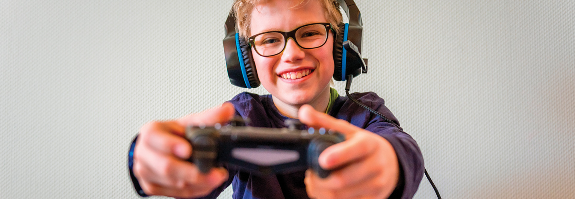 boy with glasses wearing headphones and holding gaming controller