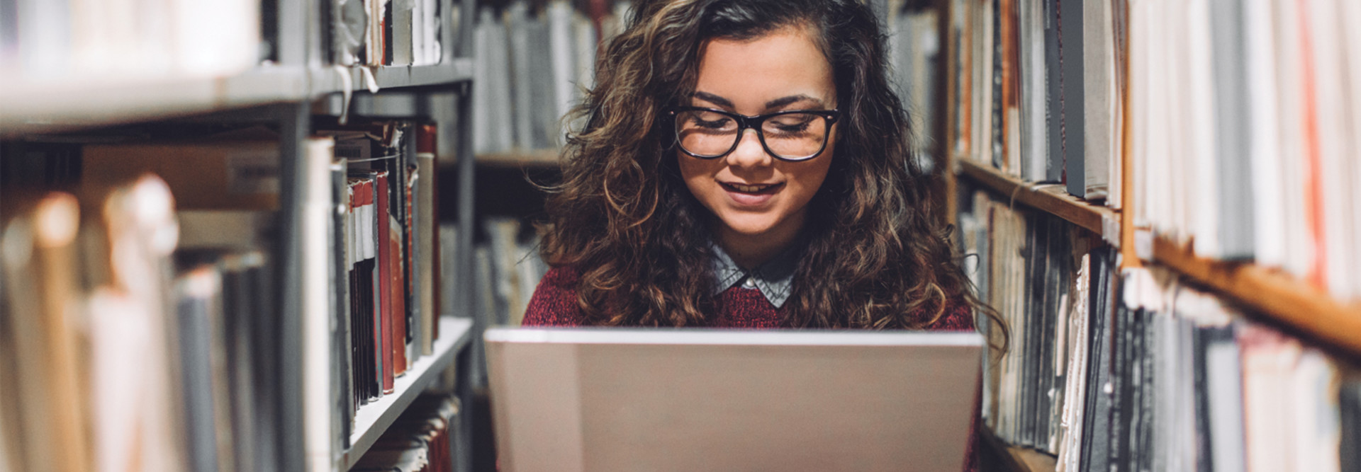 Student on laptop among stacks of books