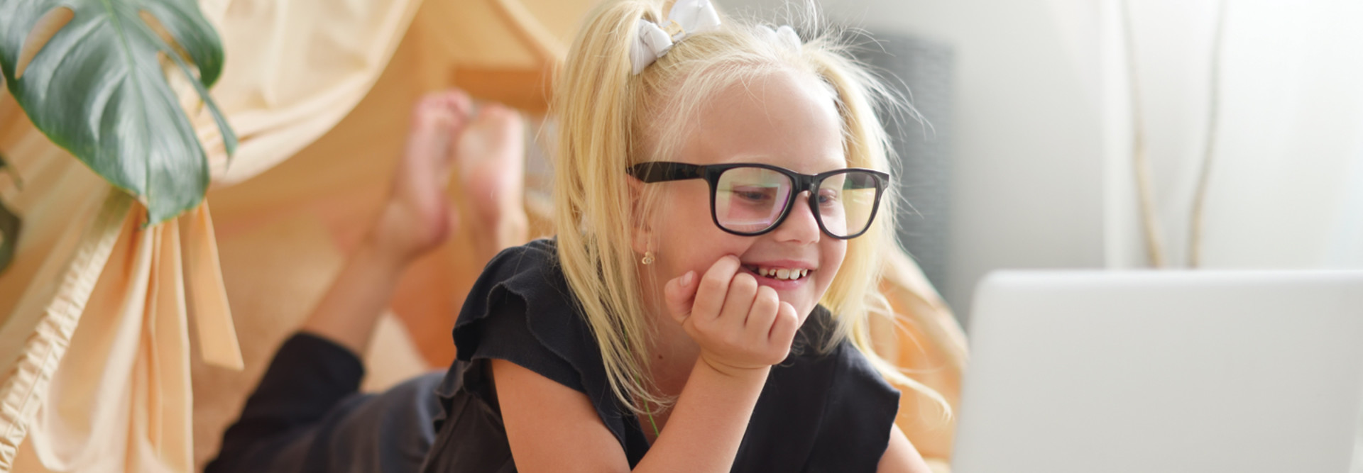Young female student with black glasses looks happily at a computer screen