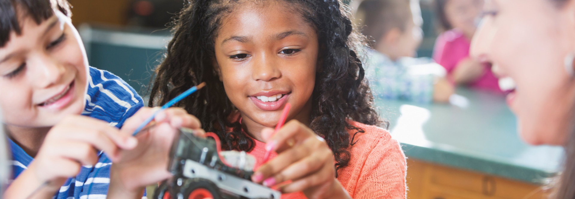 Students engage in STEM lessons with a robotic car while smiling teacher looks on