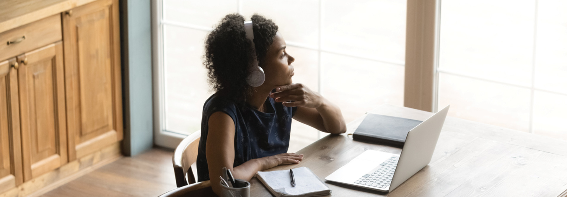 Teacher sitting alone looking out window with laptop and headphones