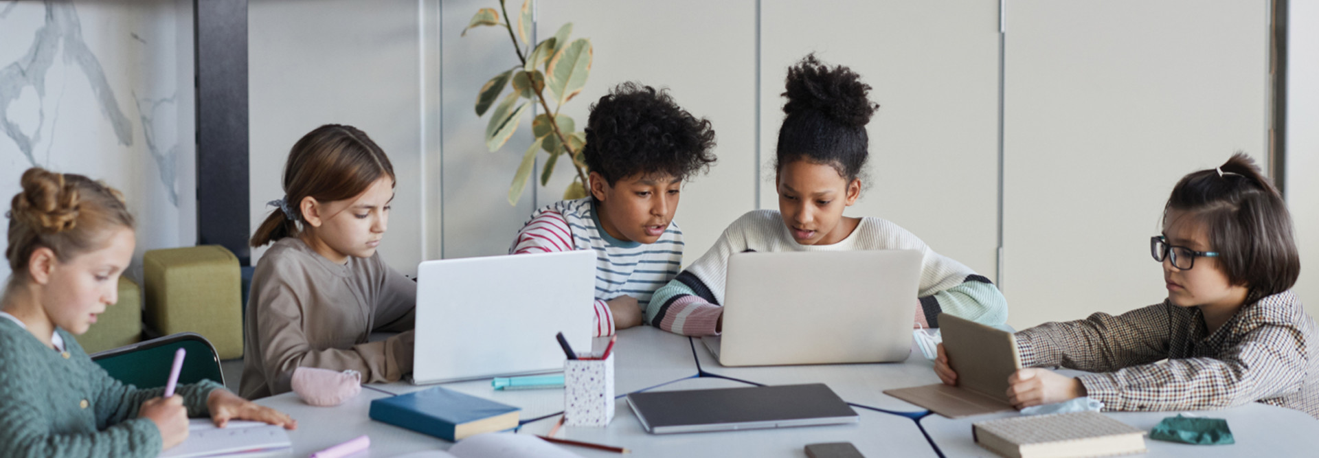 K–12 students on laptops together at a table studying