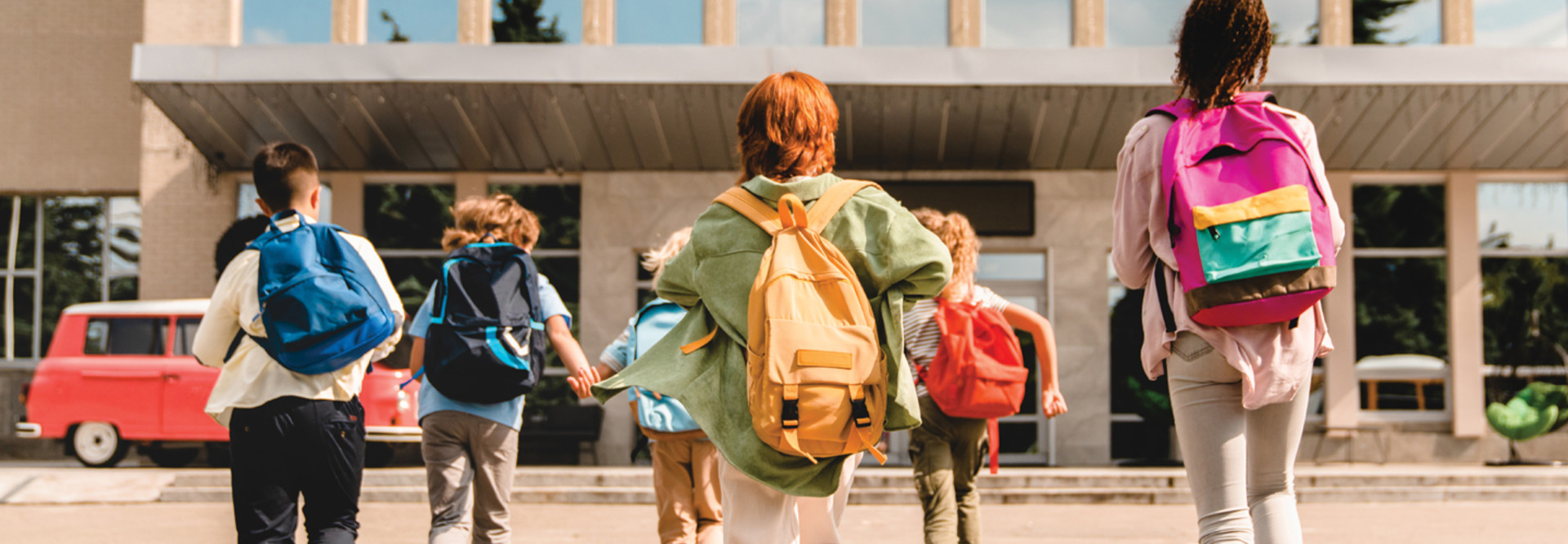 group of k-12 students with backpacks going into school building