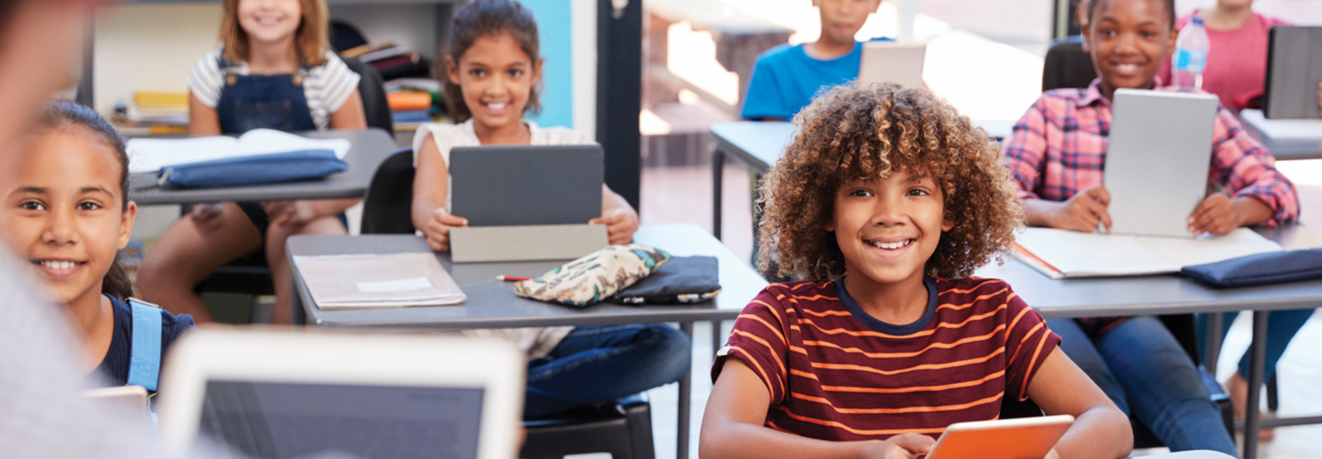 Students in classroom on tablets looking at teacher