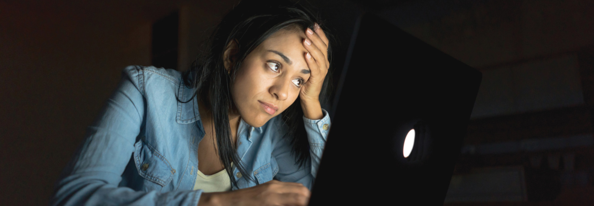 student sitting in the dark looking upset at computer screen