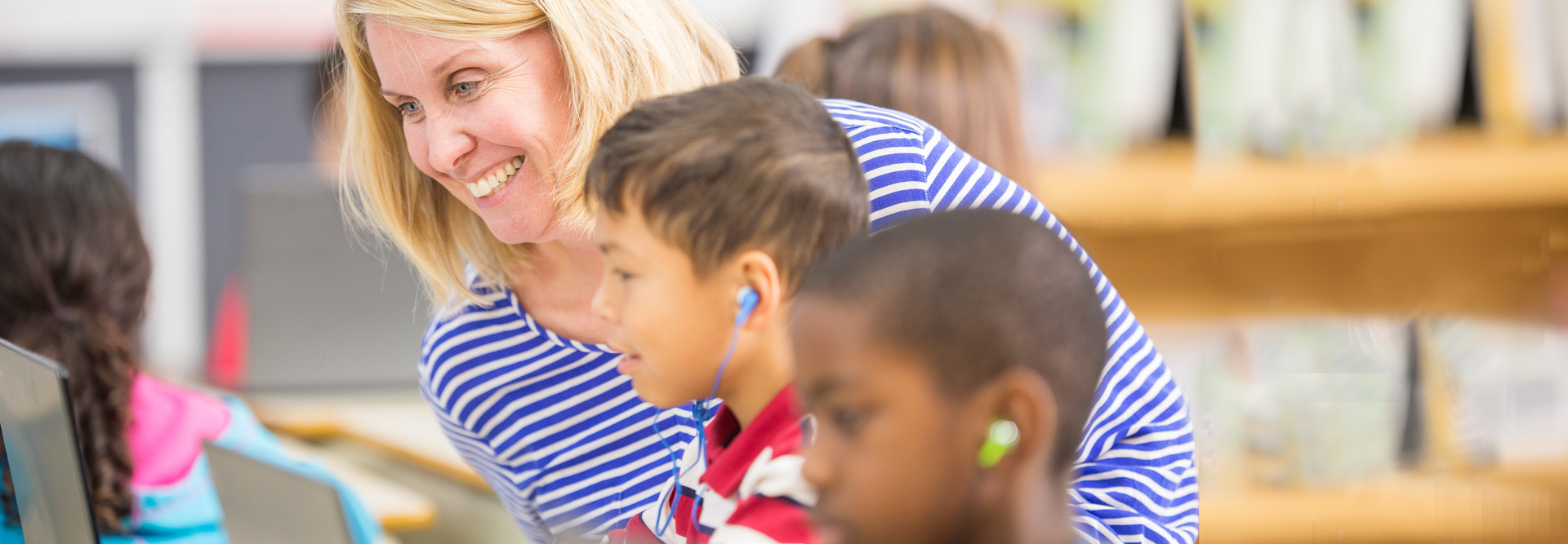 Woman teaching kids to use laptop