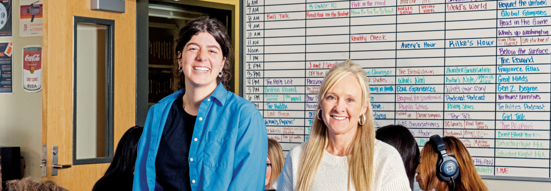 People in a classroom in front of a radio station scheduling board