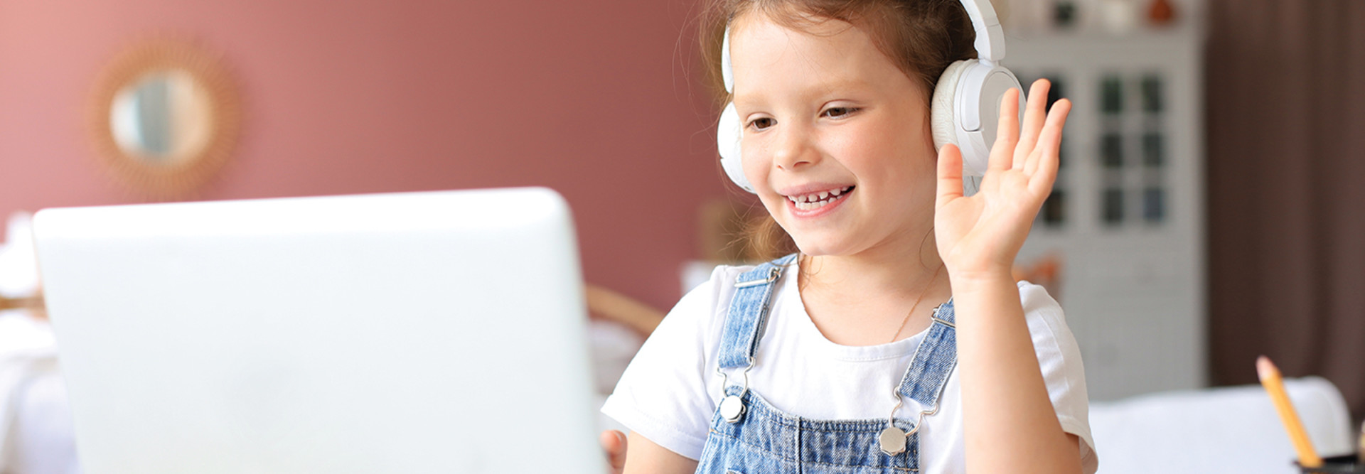 girl in headphones waving at computer screen 