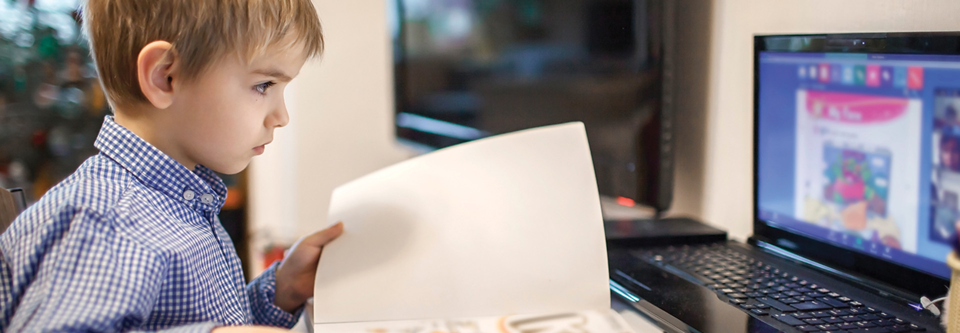 boy opening book while looking at computer screen for school