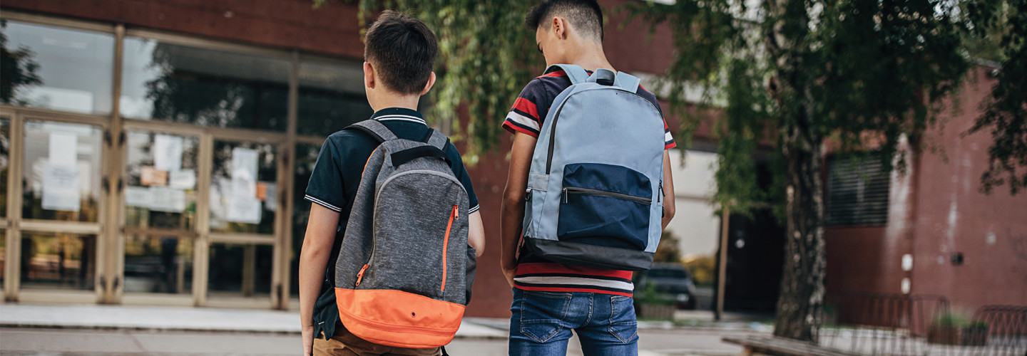 Two boys approach a school wearing backpacks