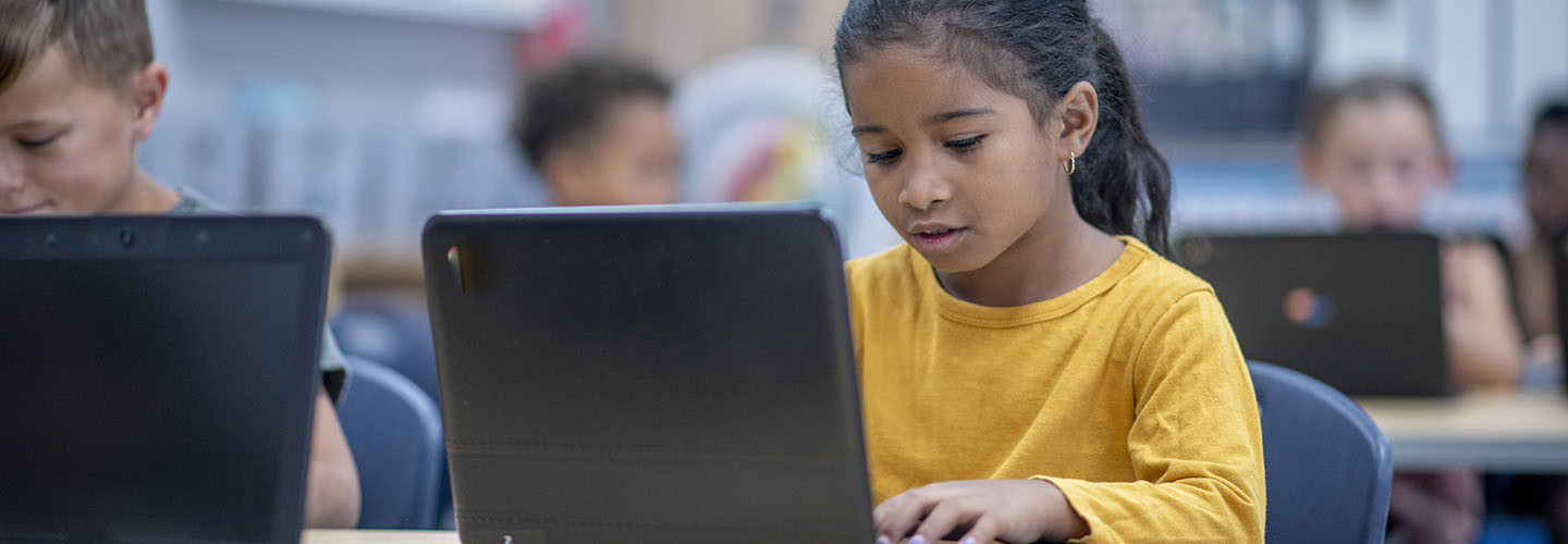 elementary students sit at their desks with personal laptops