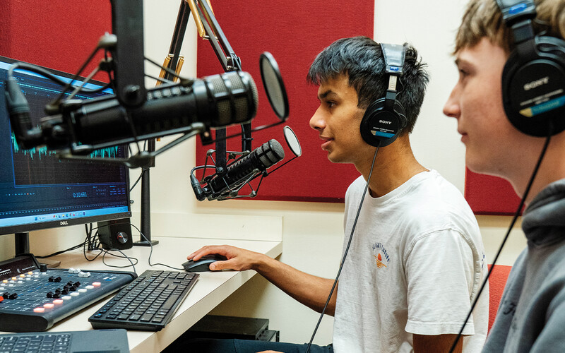 High school students sitting at microphones and a computer creating a podcast