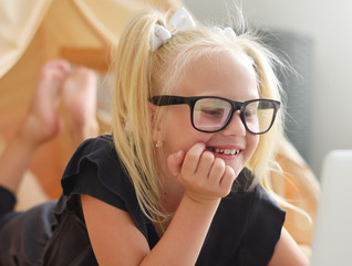 Young female student with black glasses looks happily at a computer screen