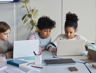 K–12 students on laptops together at a table studying