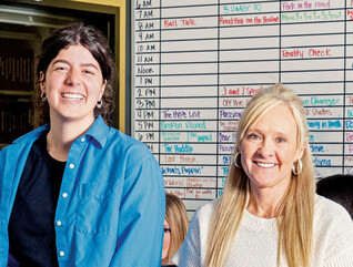 People in a classroom in front of a radio station scheduling board