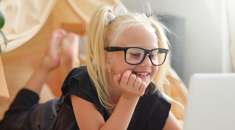 Young female student with black glasses looks happily at a computer screen