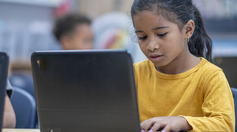elementary students sit at their desks with personal laptops