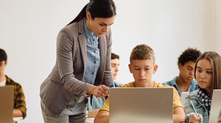 teacher helping students use laptops for school lessons