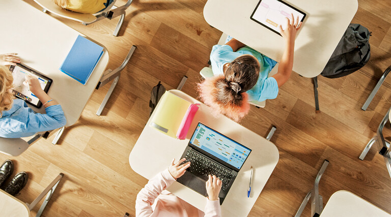 Overhead view of children sitting at desks working in a classroom on computers