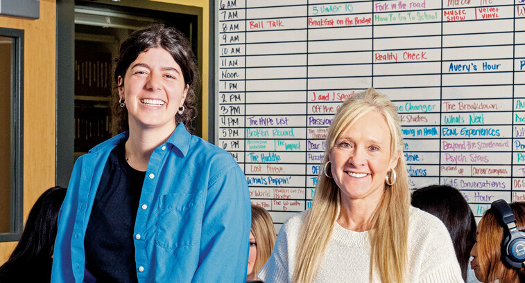People in a classroom in front of a radio station scheduling board