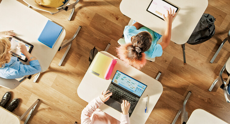 Overhead view of children sitting at desks working in a classroom on computers