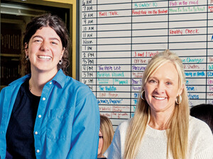 People in a classroom in front of a radio station scheduling board